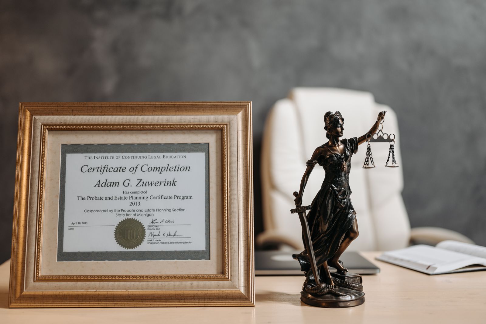 A framed certificate beside a Lady Justice figurine on a desk